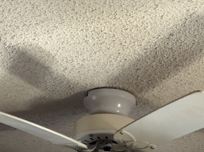 A yellowish white ceiling with popcorn on it. There is a ceiling fan as well. remove